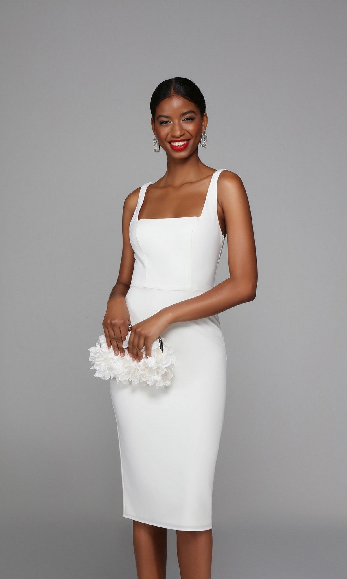 A woman in the Alyce 70010 knee length semi-formal dress holds a white ruffled clutch, smiling against a plain gray background.